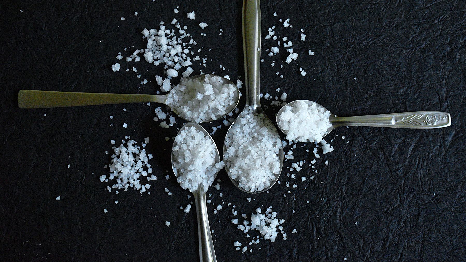 Sea salt measured on spoons against dark stone