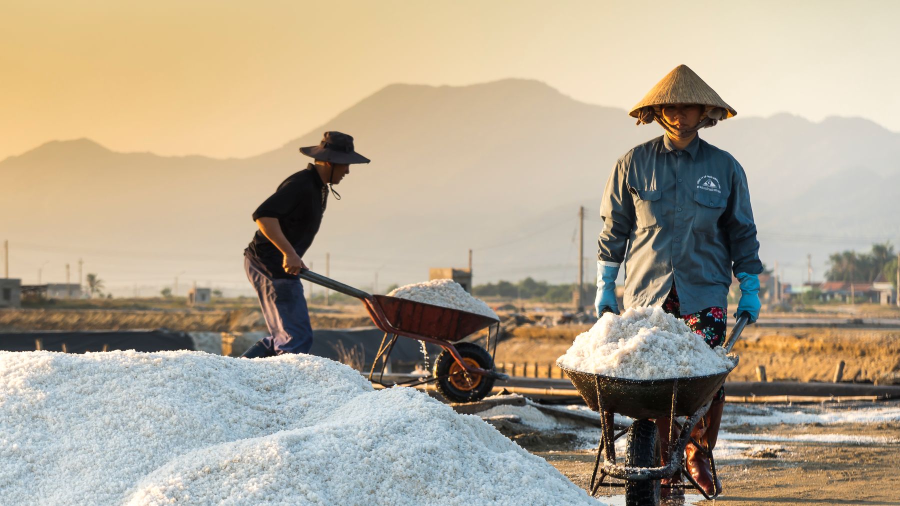 Two salt makers gathering salt at sunrise
